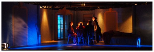 (Image: A View of the Entire Room with Actors
        Seated at a Round Table)