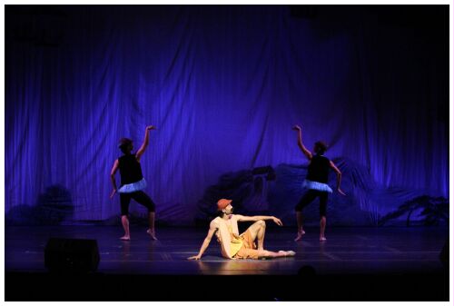 (Image: A Single Dancer is Lit at Centre Stage with Two
  Dancers behind)