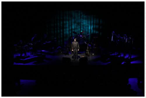 (Image: The Band is Bathed from Behind in Deep Blue
 while `Roy' Sings without Guitar)