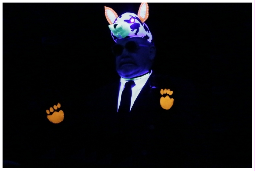 (Image: A Single Actor Glows with his Dog Mask,
  Paw Emblems on his Palms, and His White Shirt)