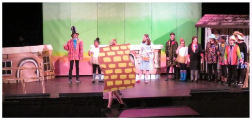 (Image: The Munchkins Build the Yellow Brick Road
  while Dorthy Speaks with the Mayor)